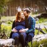 Paar sitzt im Wald für ein Babybauchshooting.